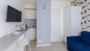 A compact kitchenette with a microwave, a small sink, and a white cabinet. There is a blue sofa and a white chair in the living area. - Italianway - The B Village Business - A22 (Milan)