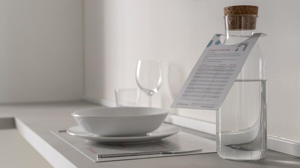A clear glass bottle with a cork stopper, a menu card attached to it, a white bowl, and a wine glass on a table. - Italianway - The B Village Business - A23 (Milan)