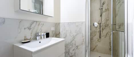 Un baño moderno con lavamanos de mármol, cabina de ducha de vidrio y un espejo grande.