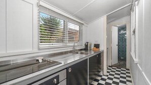 A kitchen with a stainless steel countertop, a sink, and a window with blinds. - Atlantis: retro beachside couples retreat (Currarong)