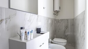 A modern bathroom with marble walls, a white sink, and toiletries. - Italianway - The B Village Business - 39 (Milan)
