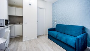 Ein modernes, kompaktes Wohnzimmer mit Küchenzeile, einem blauen Sofa und einem weißen Sessel.