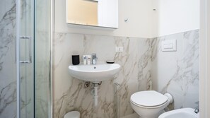 A bathroom with a marble wall, a sink, a toilet, and a glass shower enclosure. - Italianway - The B Village Standard - At03 (Milan)