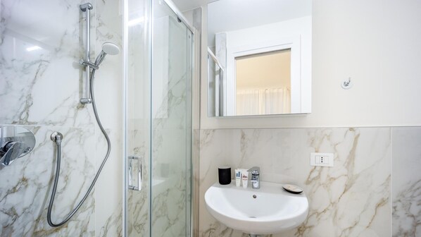 A bathroom with a glass-enclosed shower, a white sink, and a mirror above the sink. - Italianway - The B Village Standard - At03 (Milan)
