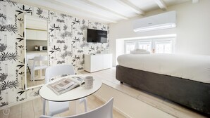 A modern bedroom with a bed, a TV, a small table with a magazine, and a chair. - Italianway - The B Village Standard - M7 (Milan)
