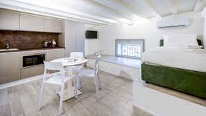 Una habitación de hotel moderna con cama, un pequeño rincón de cocina, zona de comedor y ventana con vistas.