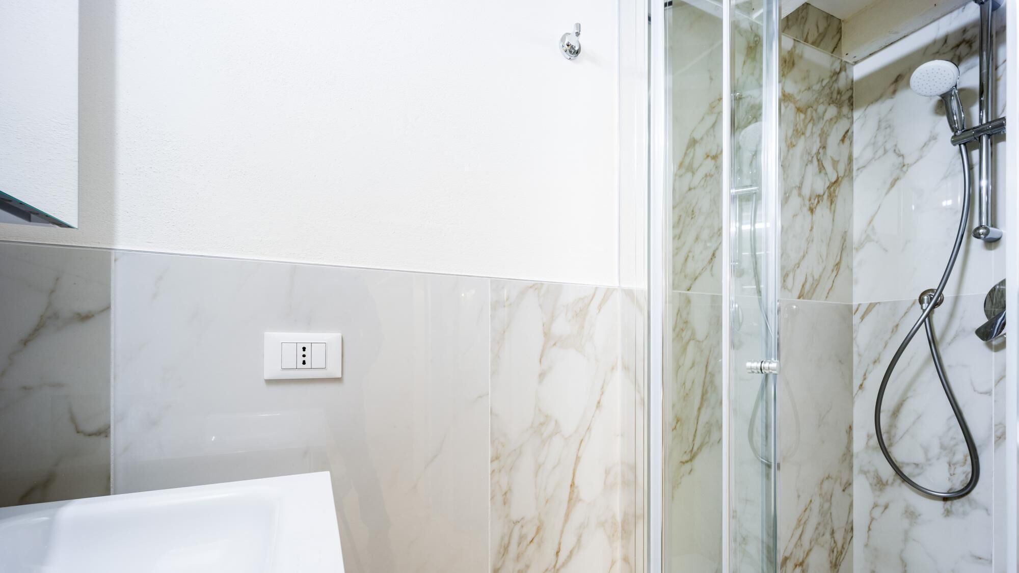 Une salle de bain avec une douche, une baignoire et un mur en marbre.