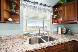 A kitchen with a granite countertop, double sink, and wooden cabinets. - Afrayed Knot Waterfront- Coastal Realty Group (Grand Isle)
