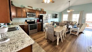 Une cuisine spacieuse dotée de meubles en bois, d’un four à micro-ondes, d’une cuisinière et d’un réfrigérateur. On y trouve également un coin repas avec une table et des chaises, ainsi qu’un salon avec un canapé et un téléviseur.