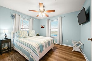 A bedroom with a bed, a ceiling fan, a TV mounted on the wall, and a window with blinds. - Afrayed Knot Waterfront- Coastal Realty Group (Grand Isle)