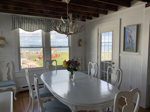 A dining area with a white table, chairs, a chandelier, and a view of the outdoors.