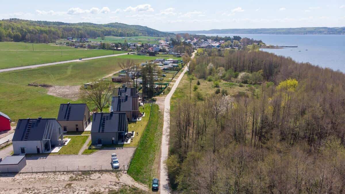 Luchtbeeld van een woongebied met huizen langs een weg, een waterpartij en groene velden op de achtergrond.