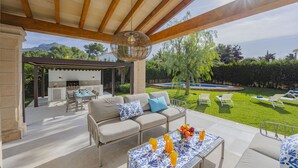 Un patio al aire libre con sofá, mesa y sillas, una zona de barbacoa y una piscina al fondo.