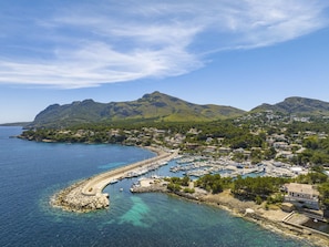 Uma cidade costeira com um porto de iates, águas azul-claras e montanhas ao fundo.