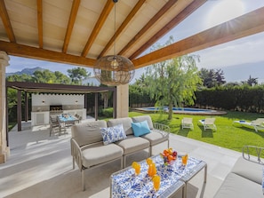 Un espace extérieur aménagé en terrasse, avec un canapé, une table garnie de fruits et une piscine en arrière-plan.