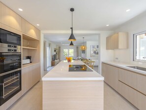 Une cuisine moderne dotée d’un îlot central, d’appareils électroménagers intégrés et de luminaires suspendus.