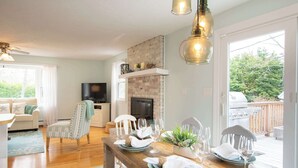 Un comedor con una mesa de madera dispuesta para cuatro personas, una chimenea de ladrillo y un televisor al fondo.