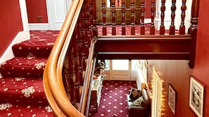 A grand staircase with a wooden handrail, red carpeted steps, and a chandelier. - Moffat Independent Hostel (Moffat)