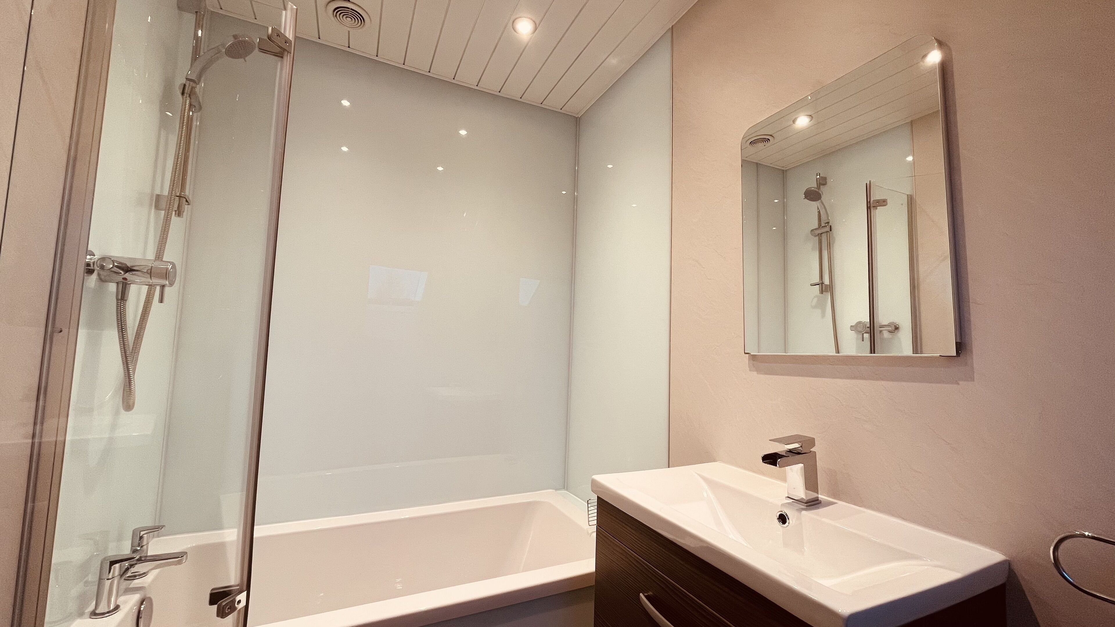 A modern bathroom with a glass-enclosed shower, a white bathtub, and a vanity with a mirror.