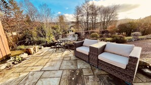 A patio area with a wicker sofa and a round table, surrounded by stone flooring and various plants. - Moffat Independent Hostel (Moffat)