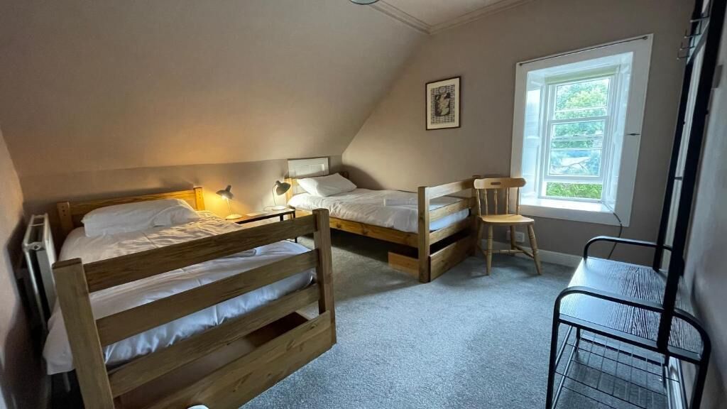 Un dormitorio con dos literas, un escritorio, una silla y una ventana que deja entrar luz natural.