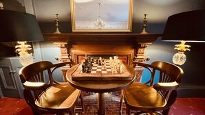 A chessboard set on a wooden table with chairs, a fireplace, and wall-mounted lamps. - Moffat Independent Hostel (Moffat)