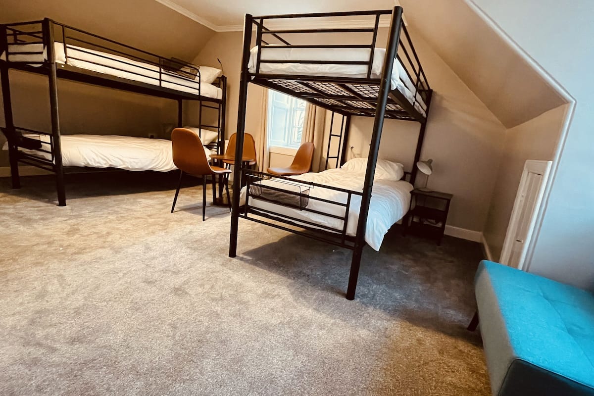Une chambre de dortoir avec des lits superposés, un bureau, une chaise et une petite table de chevet.