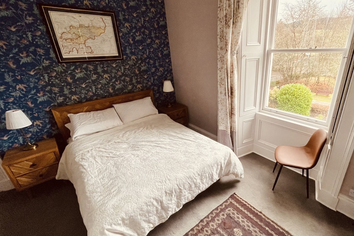 Une chambre à coucher avec un lit, une chaise, une fenêtre, une carte accrochée au mur et une lampe sur la table de chevet.