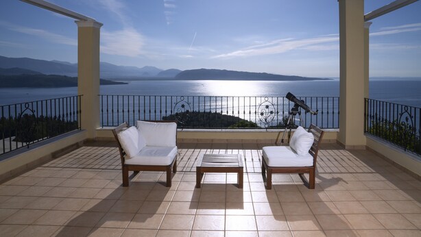 A balcony with two white cushioned chairs, a small table, and a telescope. The balcony overlooks a body of water and distant mountains. - Bellina Villa, Corfu (Αγνίτσινη)