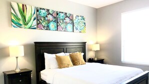 A bedroom with a bed, two bedside tables, lamps, and three floral paintings on the wall. - 301 - Super Clean & Beautiful. Pools, Gym, Lake (Orlando)