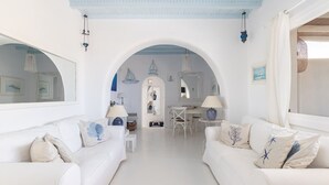 A spacious living room with white furniture, a dining area, and a view through an arched doorway. - Villa Diane (Mykonos)