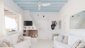 A bright, white room with two white sofas, a ceiling fan, a TV, and a door with a mirror. - Villa Diane (Mykonos)