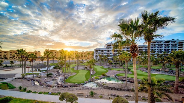 A golf course with palm trees, a water feature, and a hotel in the background. - Casa Blanca Golf Villas 2 Bedrooms Condo E 212 (Puerto Peñasco)
