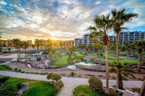 A golf course with palm trees, a water feature, and a hotel in the background.
