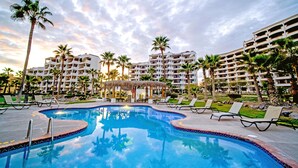 A hotel pool area with lounge chairs, palm trees, and a clear sky. - Casa Blanca Golf Villas 2 Bedrooms Condo E 212 (Puerto Peñasco)