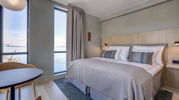 A modern hotel room with a large bed, a dining table, and a view of the sea.