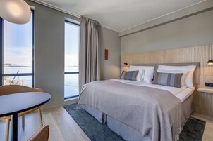 Una habitación de hotel moderna con una cama grande, una mesa de comedor y vista al mar.
