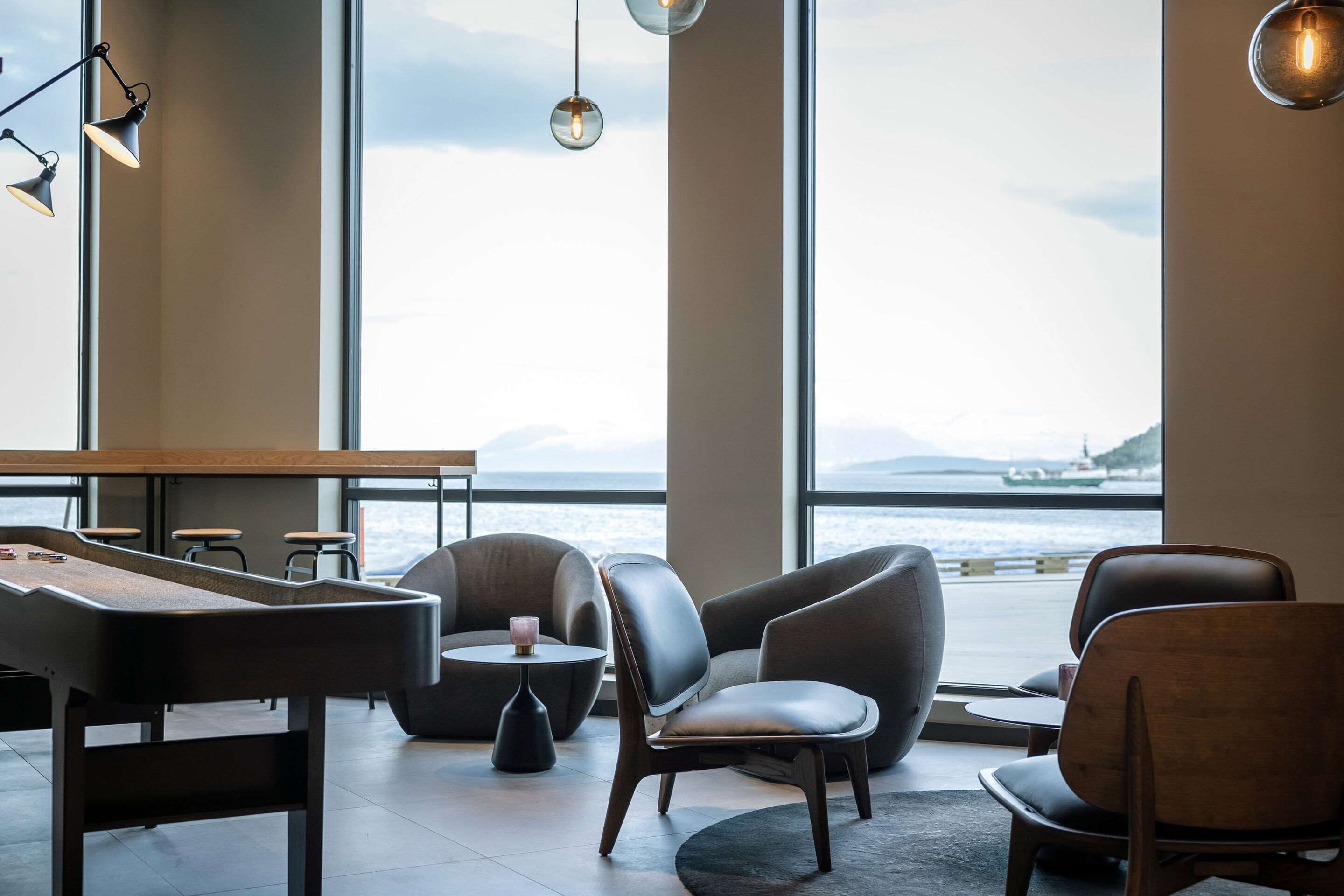 Ein stilvoller Lounge-Bereich mit Billardtisch, Ledersesseln und großen Fenstern mit Blick auf ein Gewässer.