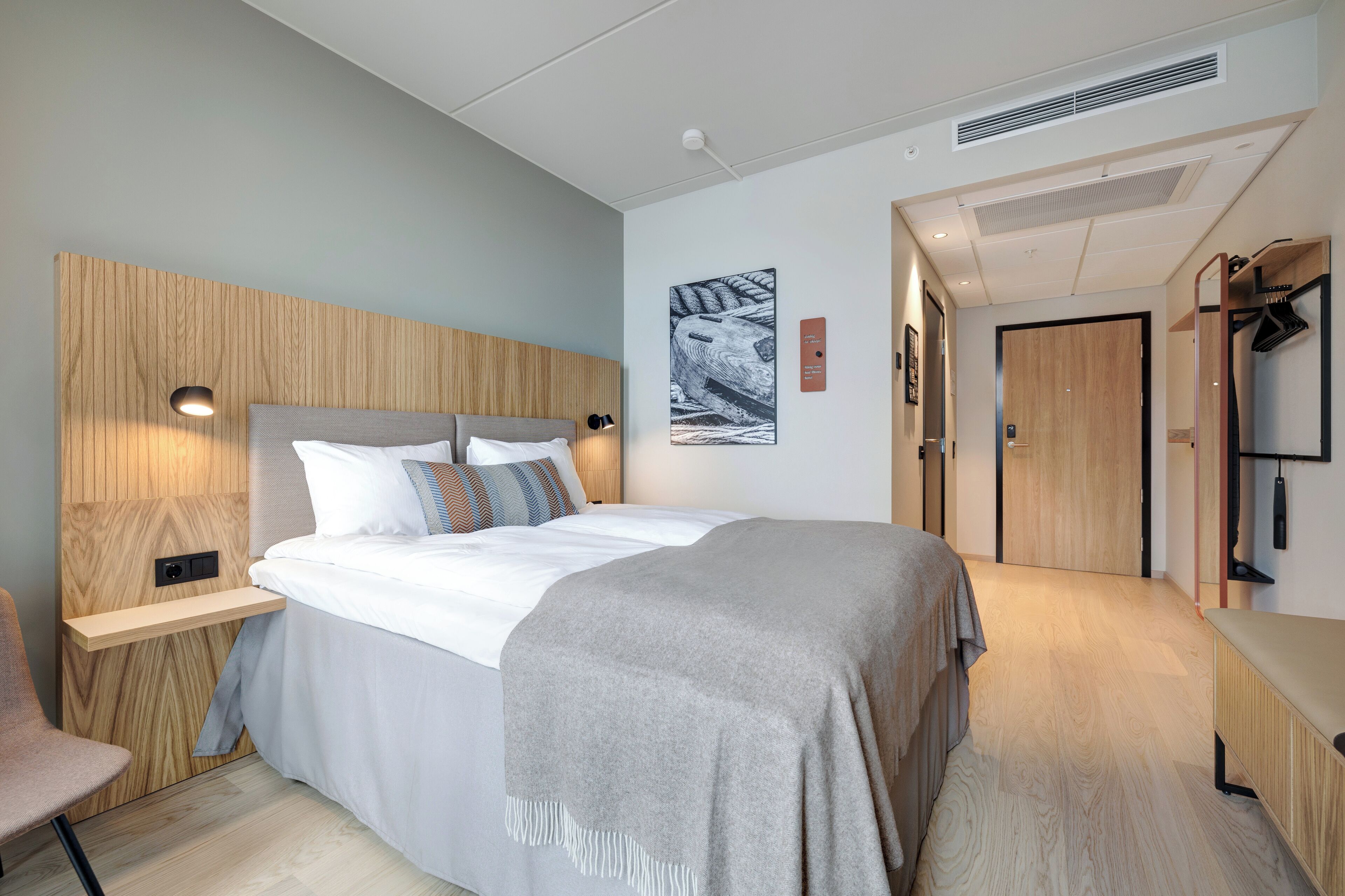 A modern bedroom with a wooden headboard, a bed with white linens, a bedside table, and a chair.