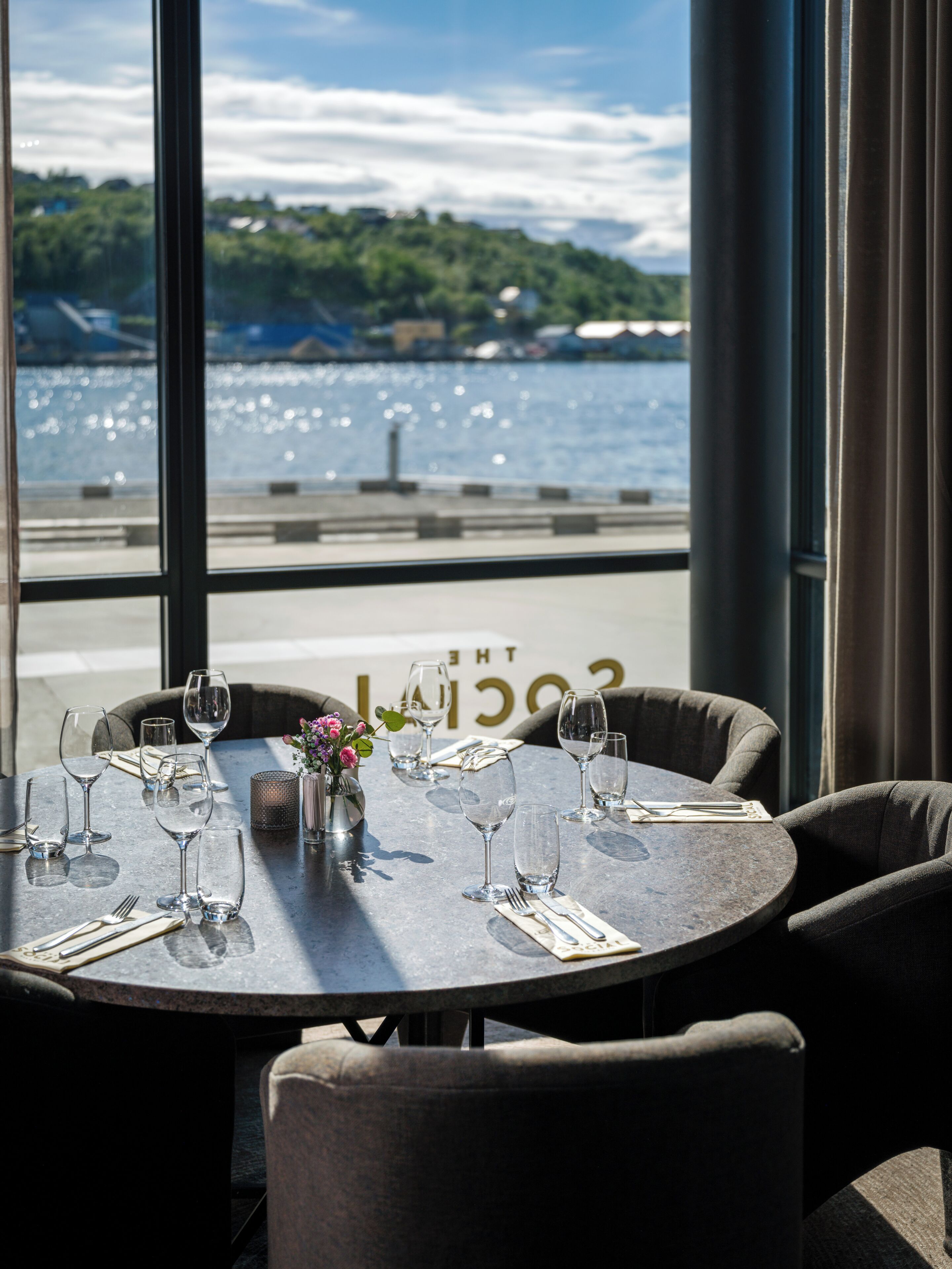 Una mesa lista para comer con vista al agua y follaje en el fondo.