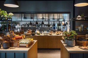 Una barra de desayuno moderna con diversas opciones de comida y bebidas, detalles de madera y plantas en macetas.