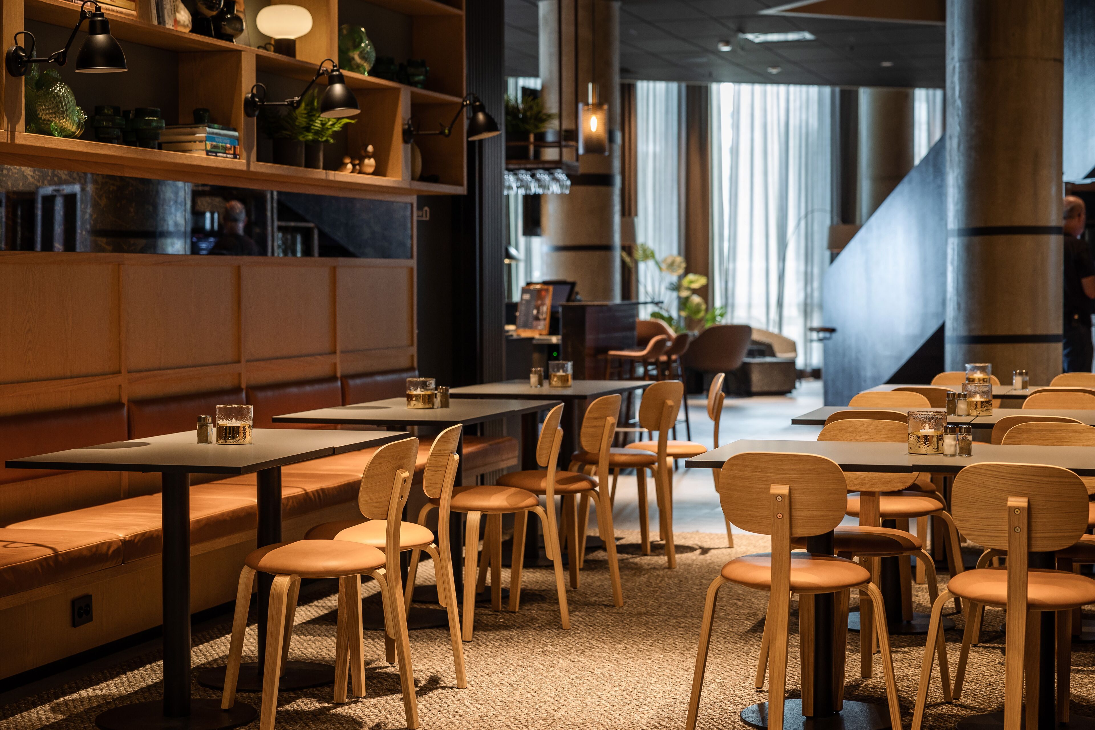 Un interior de restaurante moderno con mobiliario de madera, lámparas colgantes y vistas a la calle.