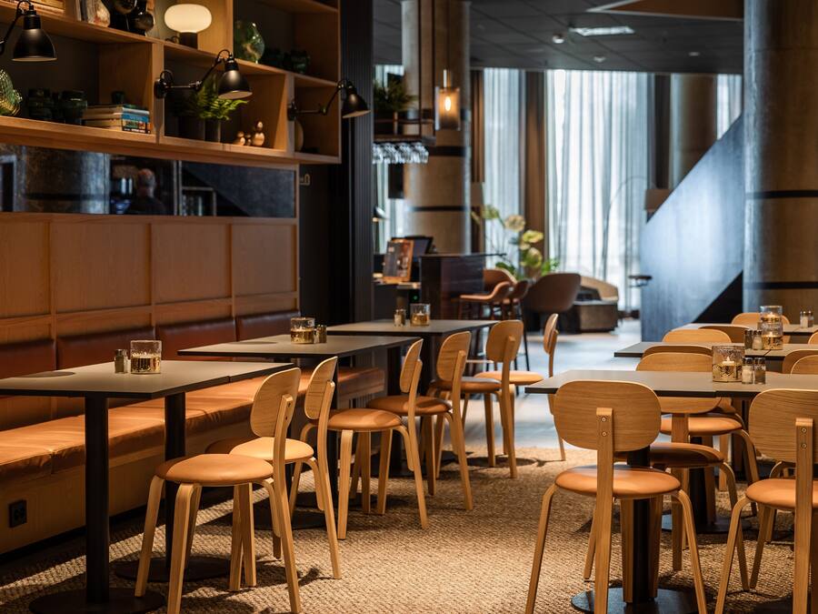 Un interior de restaurante moderno con mobiliario de madera, lámparas colgantes y vistas a la calle.