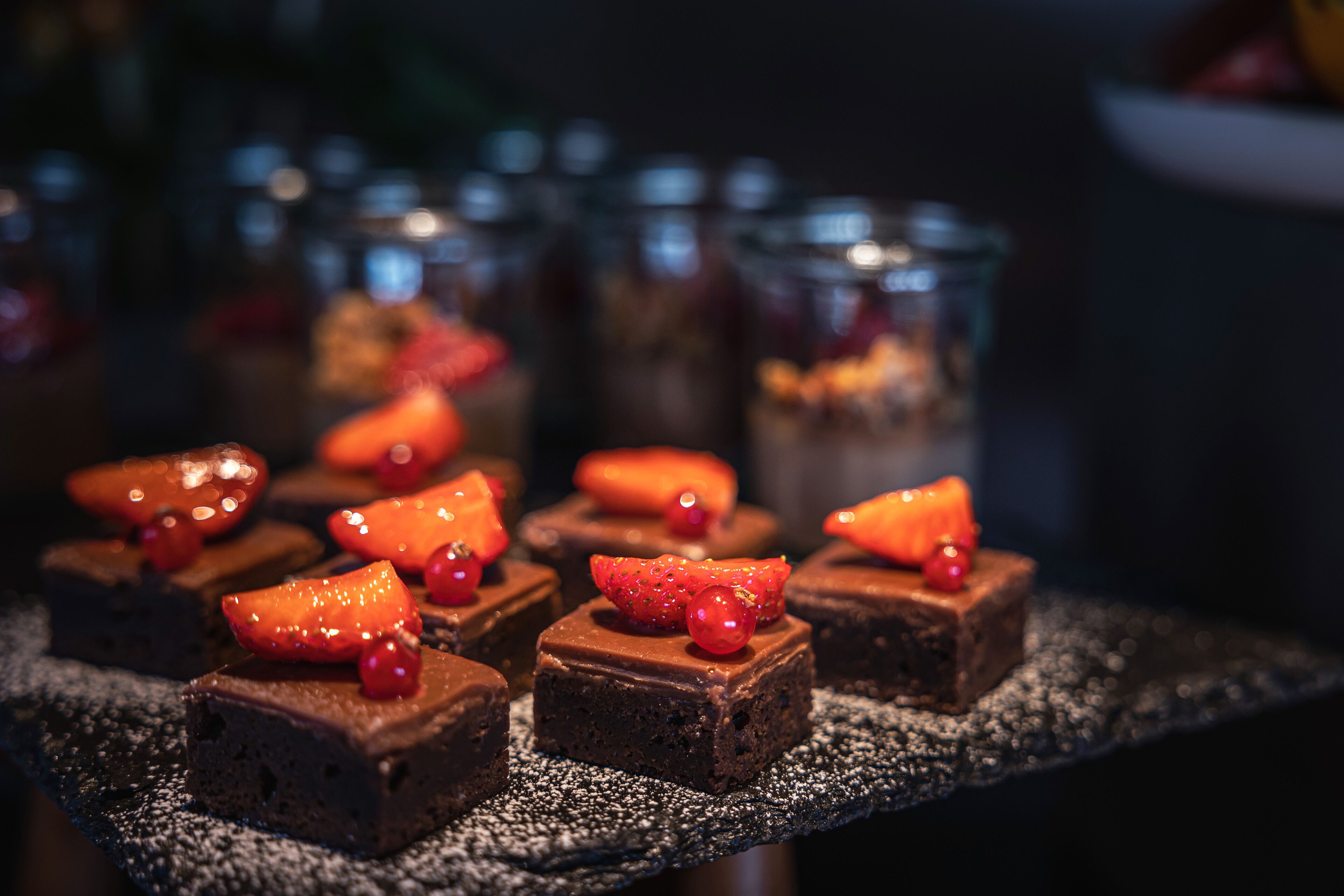 Una presentación de postres con brownies cubiertos de fresas y frutos rojos.