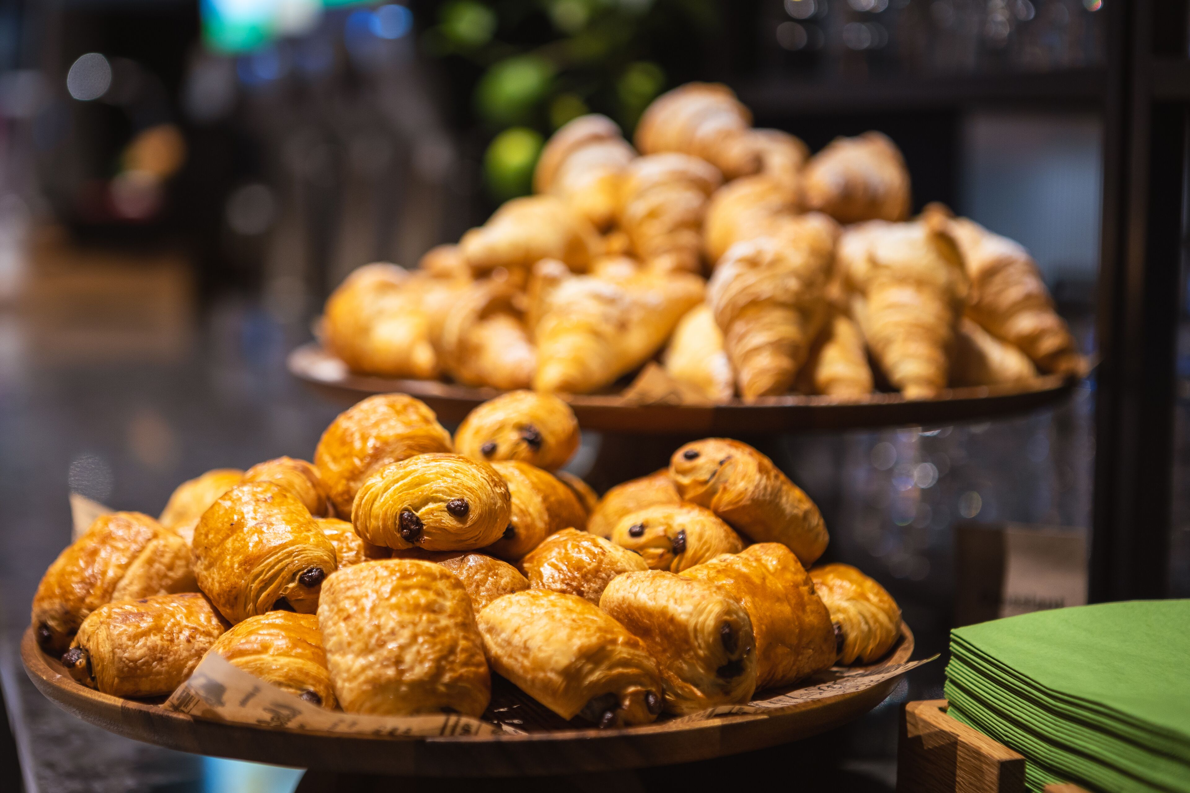 Due vassoi di legno colmi di paste assortite, probabilmente croissant e altri prodotti da forno, esposti in una panetteria o caffetteria.