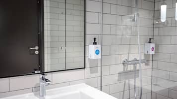 Une salle de bain moderne avec un lavabo blanc, une cabine de douche en verre et deux distributeurs de savon fixés au mur.