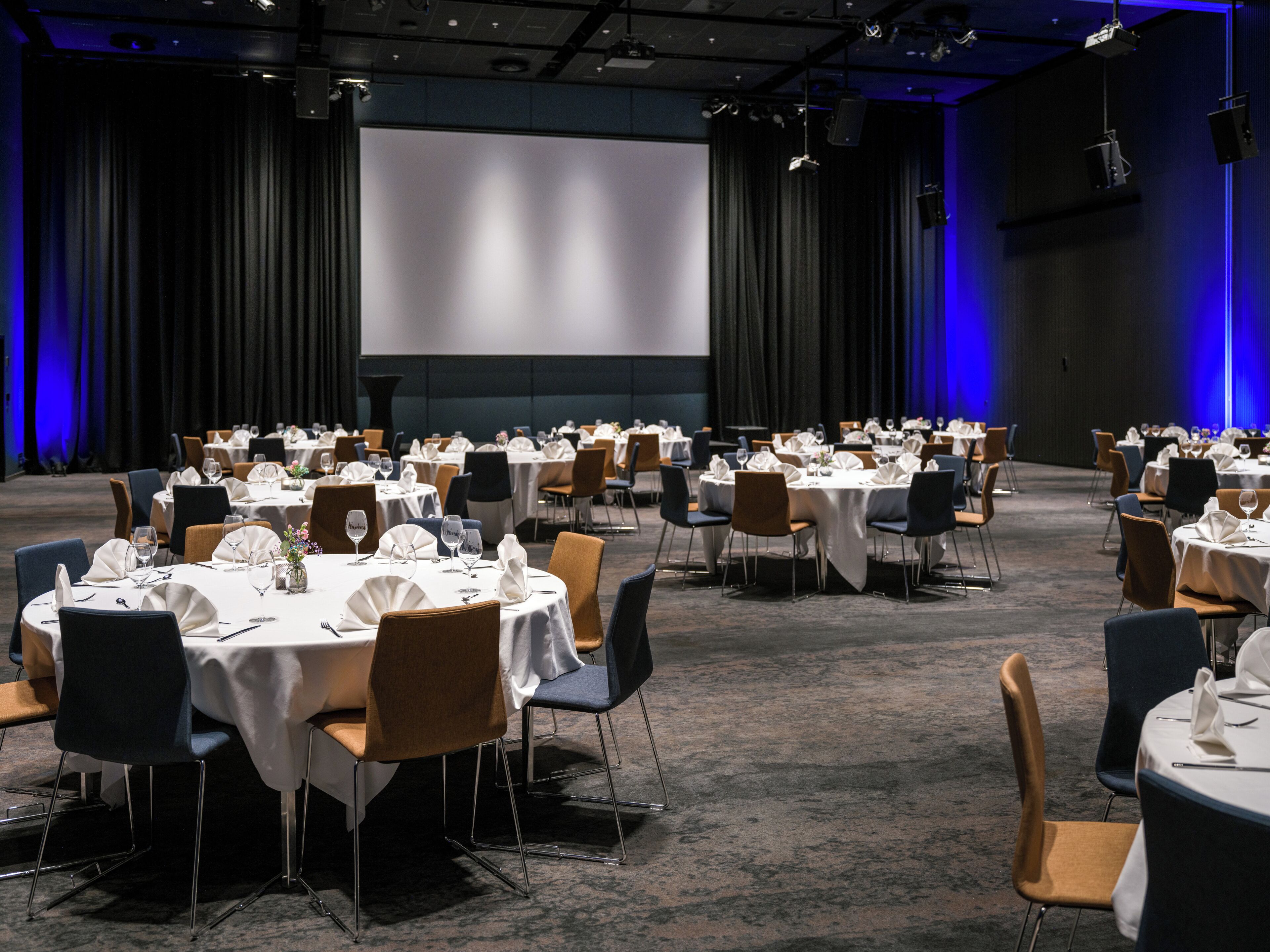 A conference room with multiple tables set for dining, arranged in rows with chairs.