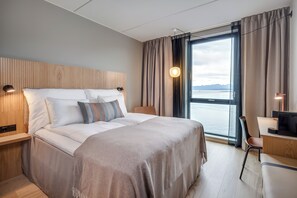 Una habitación de hotel moderna con una cama grande, un escritorio y vistas al mar.