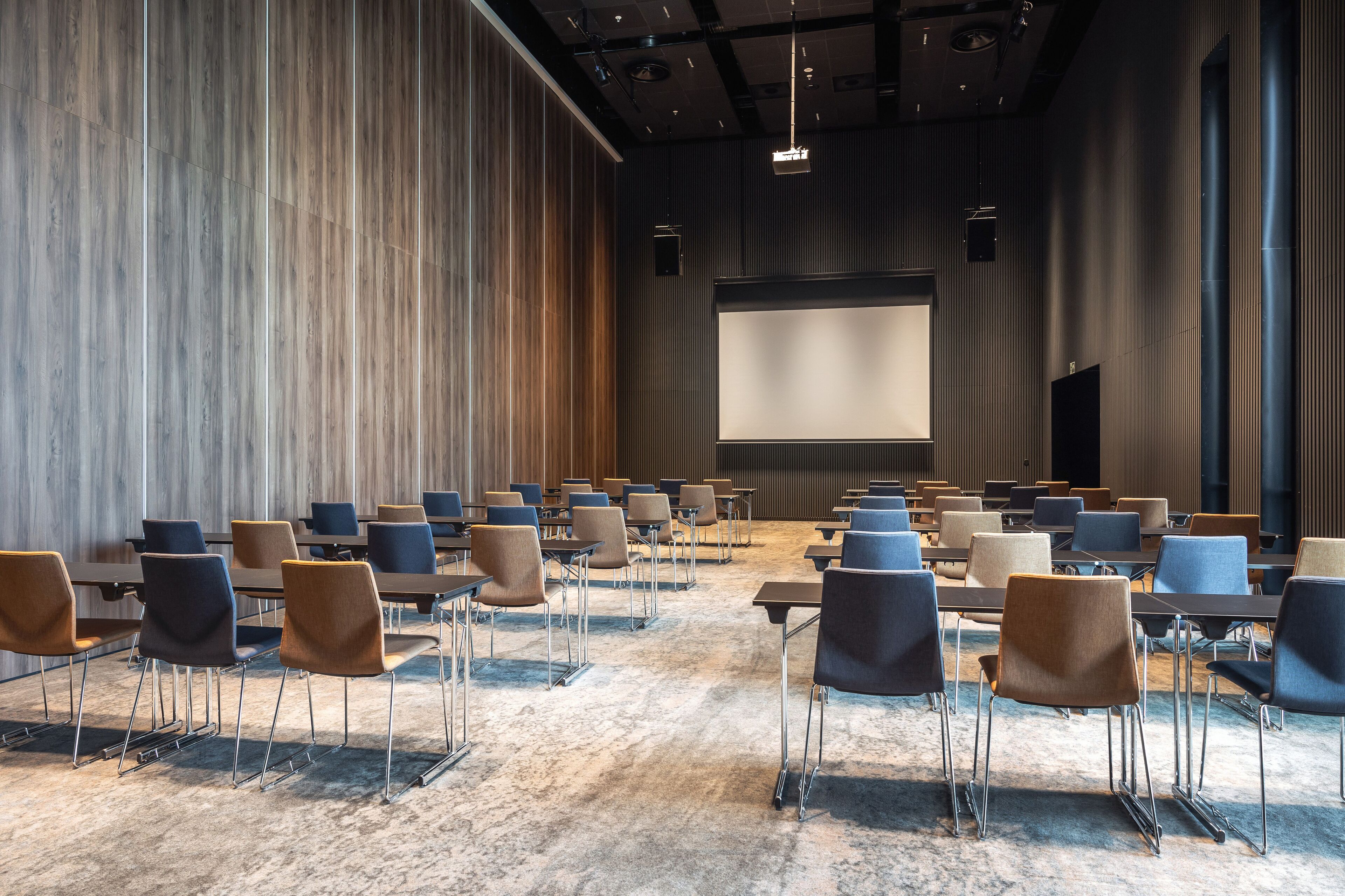 Un salón de conferencias con filas de sillas y mesas, una pantalla grande y un revestimiento de pared de madera.