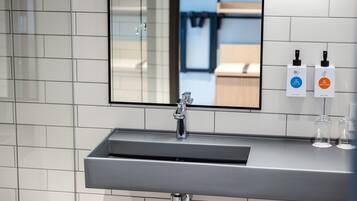 A modern bathroom with a rectangular sink, a mirror, and two hand sanitizer bottles on the wall.